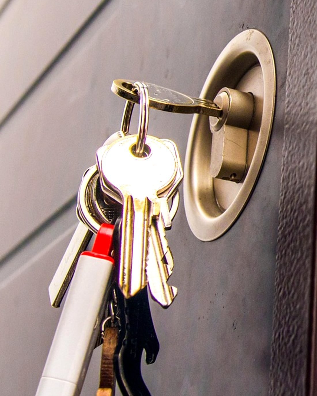 A bunch of keys hanging from the key left in the cylinder of a grey steel door