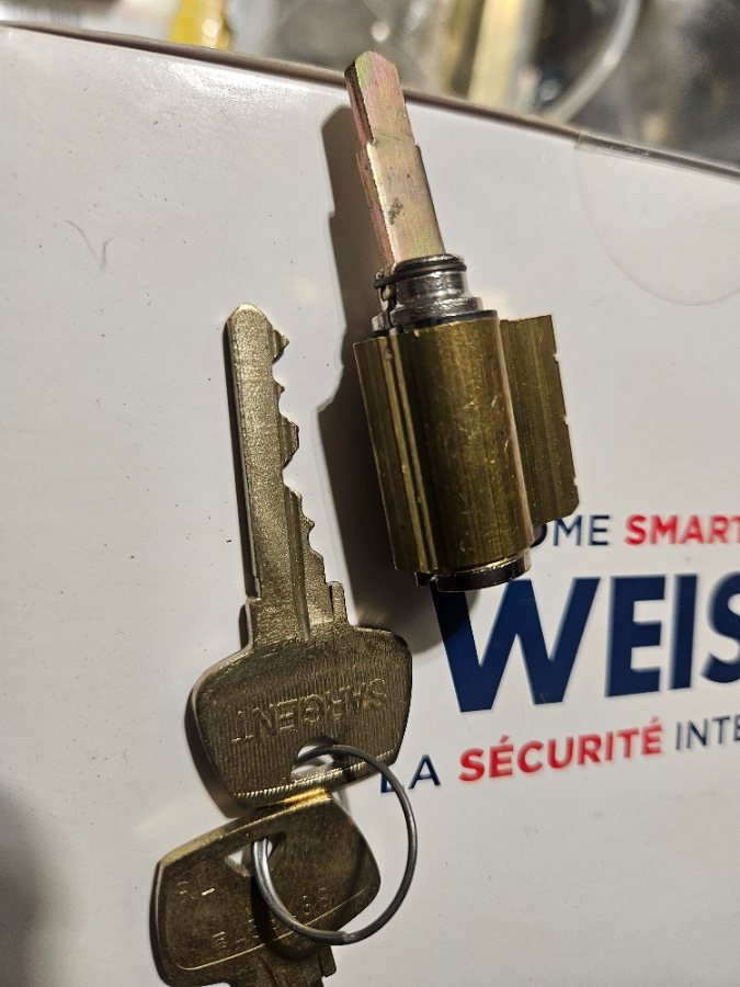 A brass Sargent lock cylinder and its keys resting on a white workbench