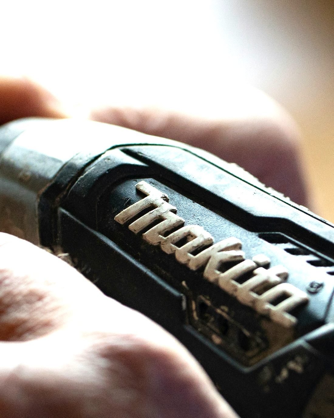 A hand closed around the body of a black cordless drill