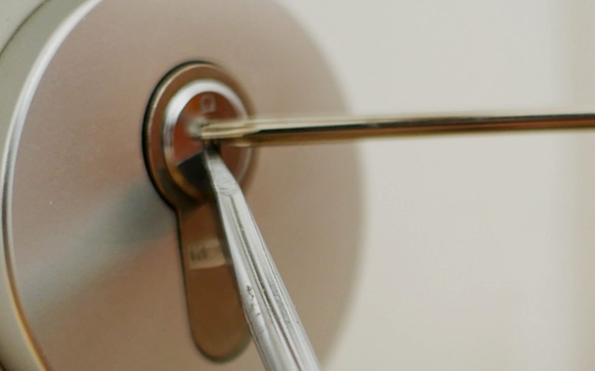 Close view of a round cylinder lock on a white door with a slim tension tool in the keyway